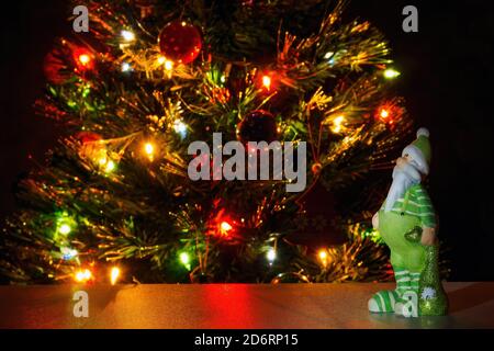 Statuina di Babbo Natale in abiti verdi sullo sfondo albero di natale con luci di ghirlanda. Copia testo, messa a fuoco selettiva Foto Stock