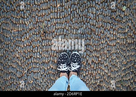 gambe in sneakers e jeans, su strada pavimentata con pietre, vista dall'alto Foto Stock