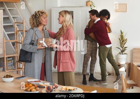 Gruppo di eleganti adulti si salutano e si scambiano regali mentre gli ospiti sono ospitali al party a cena all'interno Foto Stock