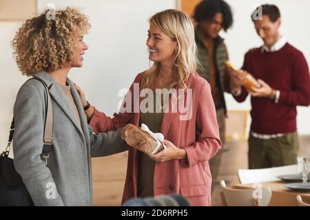 Vista laterale a un gruppo di eleganti adulti che salutano ciascuno altri e scambiando regali mentre accoglie gli ospiti alla festa di cena all'interno Foto Stock