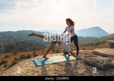 Vista laterale completa del corpo di una femmina sottile che fornisce supporto a. Partner maschile durante l'esecuzione tre zampe rivolto verso il basso Dog posa mentre si pratica yoga togeth Foto Stock