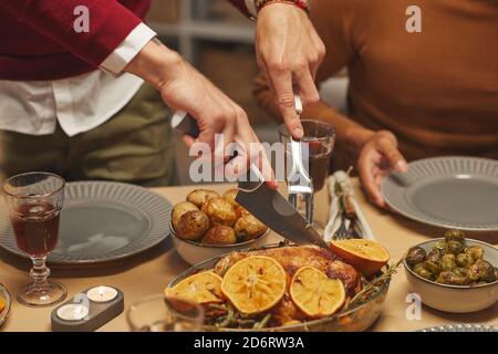 Primo piano di un uomo irriconoscibile che taglia delizioso pollo arrosto mentre si gusta la cena del Ringraziamento con amici e familiari, copy space Foto Stock