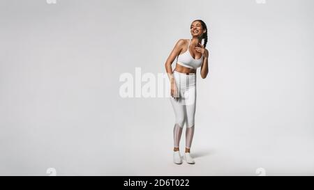 Donna in forma fisica indossare isolato su sfondo bianco. Donna sorridente in forma che si rilassa durante l'allenamento guardando via. Foto Stock