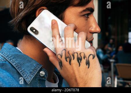 Vista laterale closeup del giovane maschio raccolto con tatuaggio conversazione manuale sul telefono cellulare Foto Stock