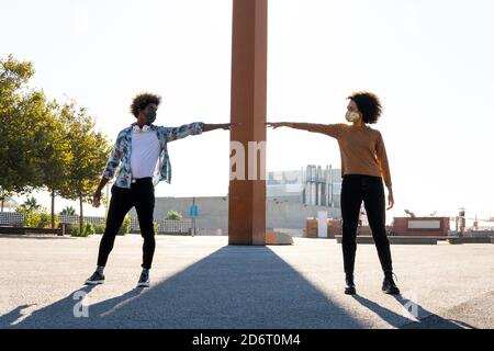 Anonimo uomo nero trendy in maschera con Afro acconciatura che raggiunge braccio a partner femmina sulla strada mentre si guarda ciascuno altro durante il periodo di quarantena Foto Stock