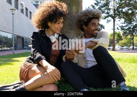 Allegro giovane afroamericano uomo e ragazza seduta sul prato nel parco Foto Stock