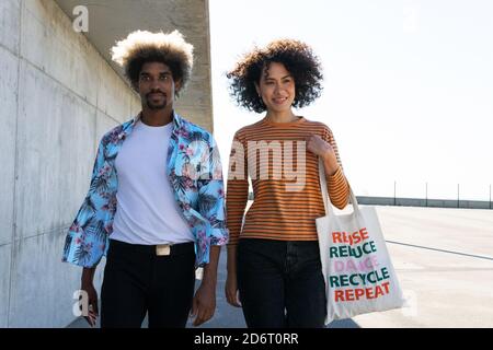 Giovane uomo e donna nero elegante con borsa riutilizzabile camminare insieme sulla strada nelle giornate di sole Foto Stock