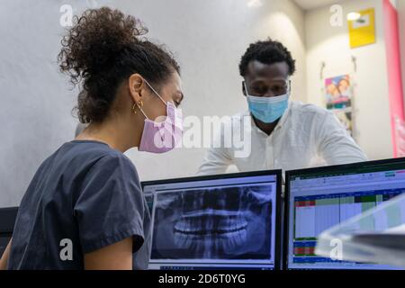 Vista laterale della femmina nera medico in maschera medica esame Raggi X sul monitor del computer mentre si lavora in moderno clinica dentale Foto Stock