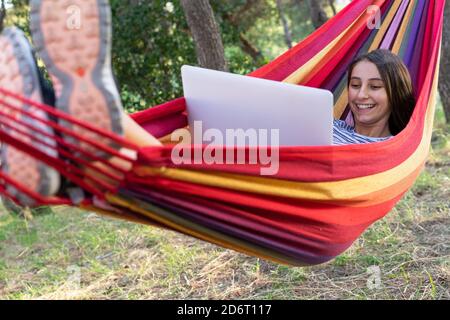 Ragazza felice freelance che si trova in amaca e digitando su netbook mentre si lavora al progetto di avvio Foto Stock