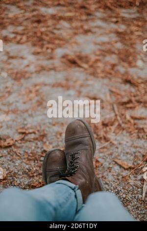 Gambe in stivali da trekking di uomo anonimo seduto nel parco con foglie caduto il giorno d'autunno Foto Stock