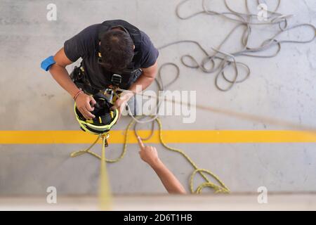 Vista dall'alto di un irriconoscibile pompiere con casco e corda vicino ritagliare il collega puntando con il dito durante la pratica sul lavoro Foto Stock