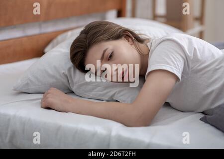 Giovane donna sdraiata da sola nel suo letto, lutto per la perdita della persona amata, che soffre di grave depressione Foto Stock