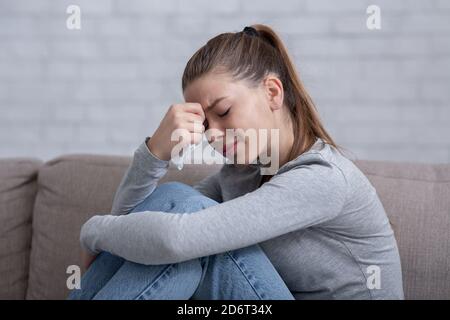 Donna solitaria millenaria che si sente disperata o disperata, piangendo sul divano a casa Foto Stock