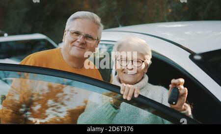 La coppia senior ha acquistato una nuova auto. In piedi vicino alla porta e donna che tiene le chiavi. Foto di alta qualità Foto Stock
