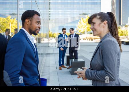 Vista laterale di giovani colleghi multirazziali positivi in abiti di classe stare insieme per strada e discutere di strategia aziendale dopo il lavoro Foto Stock