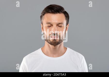 Uomo di mezza età con occhi chiusi su sfondo grigio dello studio Foto Stock