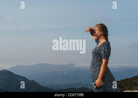 Vista laterale positiva giovane femmina con treccia in piedi su collina e godendo di paesaggi pittoreschi di nebbie alture Foto Stock