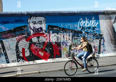 Donna giro in bicicletta Berlino muro graffiti East Side Gallery Berlino Germania Friedrichshain città arte di strada Europa città bicicletta strada Berlino bicicletta muro Foto Stock