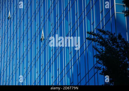 Edificio di uffici in vetro in una città. Due finestre si aprono per consentire l'ingresso di aria fresca. L'edificio in vetro degli uffici d'affari riflette il cielo blu. Foto Stock