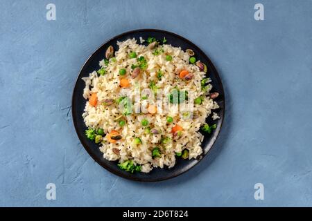 Riso vegano con verdure, sano e delizioso, colpo d'testa su uno sfondo blu Foto Stock