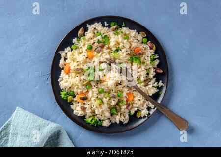 Riso vegano con verdure, sano e delizioso, il piatto è sparato dall'alto su uno sfondo blu Foto Stock