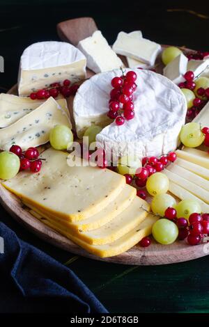 Composizione ad alto angolo di piatto di formaggi assortiti, compreso il Parmigiano Camembert E formaggi di mozzarella affettati e decorati con uve saporite e. rosso c Foto Stock