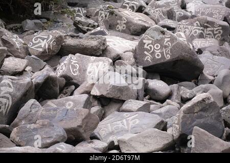 Sanscrito mantra Om mani Padme Hum inciso sulla superficie di grandi pietre grigie nel fiume di montagna nel villaggio di Baiyu in Cina Foto Stock