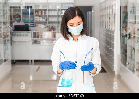 donna turca dottore o farmacista con maschera medica sul viso uso di disinfettante in farmacia Foto Stock