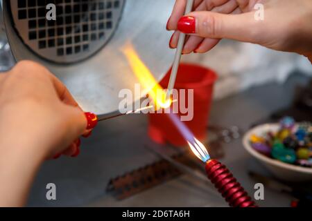 L'artista riscalda il vetro con un bruciatore a gas. Il processo di fabbricazione dei monili di vetro. Le mani del maestro si avvicinano Foto Stock