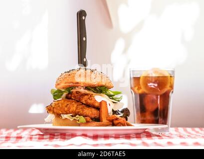 Hamburger di pollo appetitoso con verdure e cotoletta sul piatto con Patatine fritte servite a tavola con un bicchiere di coke freddo in una caffetteria rustica Foto Stock