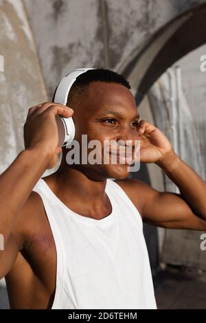 Allegro afroamericano maschio in cuffie wireless ascolto di canzoni mentre si allenano all'aperto Foto Stock