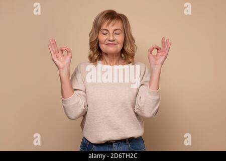 Riposante donna matura si sente rilassata, tenendo le palme insieme, cerca di concentrarsi o di essere focalizzato Foto Stock