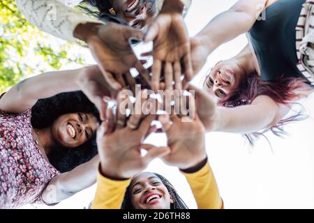 Da sotto di gruppo di donne allegre multirazziali che stanno insieme e accatastare le mani in nome dell'unità e dell'amicizia Foto Stock