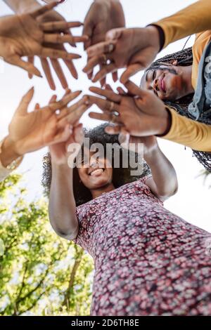Da sotto di gruppo di donne allegre multirazziali che stanno insieme e accatastare le mani in nome dell'unità e dell'amicizia Foto Stock