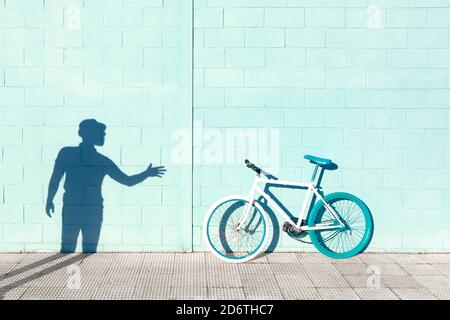 Ombra di uomo irriconoscibile sulla parete blu vicino alla bicicletta elegante parcheggiato sul marciapiede durante la giornata di sole Foto Stock