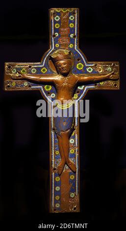 Uno smalto champlevé romanico del XIII secolo su un crocifisso dorato d'altare in rame raffigurante Cristo sulla Croce, originario di Limoges, in Francia, esposto sotto i riflettori in una mostra museale. Croce processionale in rame dorato e inciso con smalti 1220 XIII secolo 45 x 27 cm Limoges, Francia, francese, Corpus in rame dorato con smalti e gemme Foto Stock