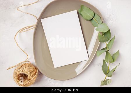 Modello di carta bianca in stile minimal. Piastra con ramificazione di carta e eucalipto su tavola di marmo. Invito di nozze, menu o altro prodotto di stampa Foto Stock