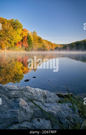 Lago Rose presso il parco statale di Hocking Hills in ohio durante l'autunno. Le foglie colorate si riflettono sull'acqua nebulosa durante la luce dell'ora d'oro all'alba. Bellissima Foto Stock