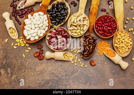 Set di legumi secchi vari in cucchiai di legno, proteina indispensabile per uno stile di vita sano. Vari tipi di fagioli. Cucina di calcestruzzo di pietra Foto Stock