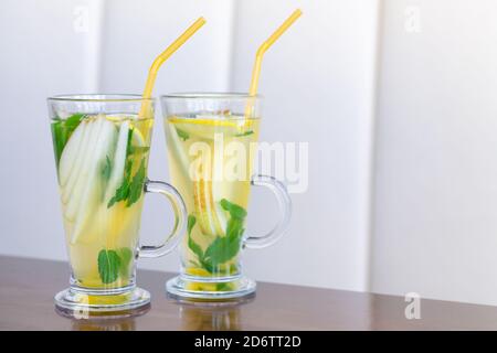 Due bicchieri di tè alla frutta con menta, limone, pera, miele e zenzero su tavolo di legno Foto Stock