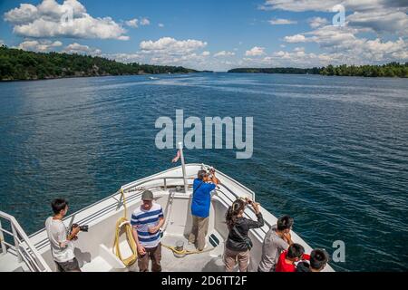 Thousand Islands Canada and US Border, luglio 2012 - passeggeri sul ponte anteriore del tour in barca per scattare foto del paesaggio panoramico Foto Stock