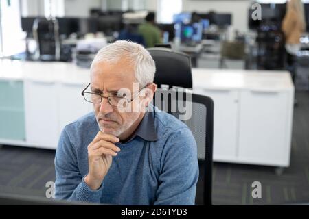 Uomo d'affari senior pensieroso seduto sulla sua scrivania in un ufficio moderno Foto Stock