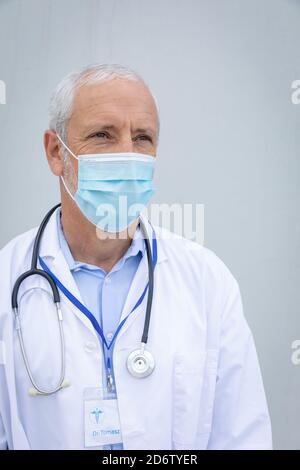 Medico maschile senior che indossa la maschera facciale su sfondo grigio Foto Stock
