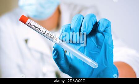 Medico che tiene il campione di test con tampone coronavirus in un flaconcino con guanti e maschera facciale in laboratorio. Primo piano Foto Stock