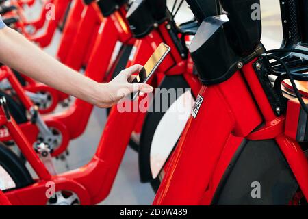 Mano di una persona irriconoscibile che utilizza il telefono per eseguire la scansione del codice QR e sbloccare una bicicletta dalla stazione di noleggio, concetto di ecologia e mobilità sostenibile Foto Stock