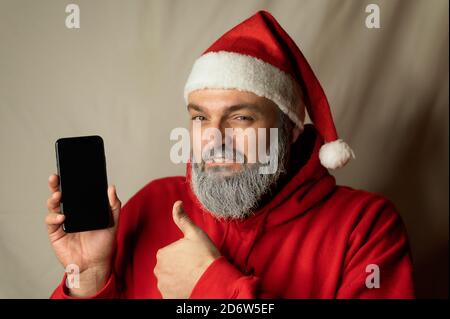 babbo natale mostra il suo cellulare e un pollice in su Foto Stock