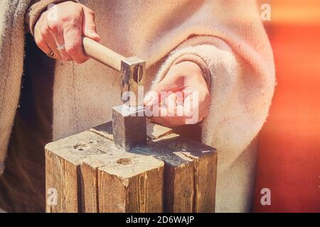 Il fabbro colpisce un piccolo martello su un foglio di ferro, stile retrò che crea denaro d'argento. Incudine e mani del maestro in abiti vintage per il prod Foto Stock