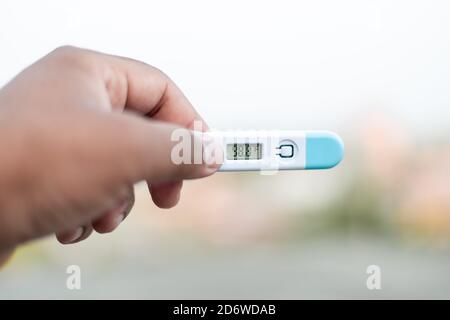 Sick Man tiene un termometro digitale con lettura della temperatura corporea in Fahrenheit vicino alla fotocamera. Foto Stock