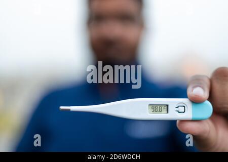 Sick Man tiene un termometro digitale con lettura della temperatura corporea in Fahrenheit vicino alla fotocamera. Foto Stock