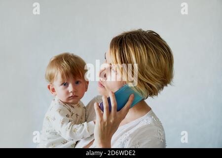 la giovane donna con un bambino tra le braccia chiede Il telefono è bianco Foto Stock